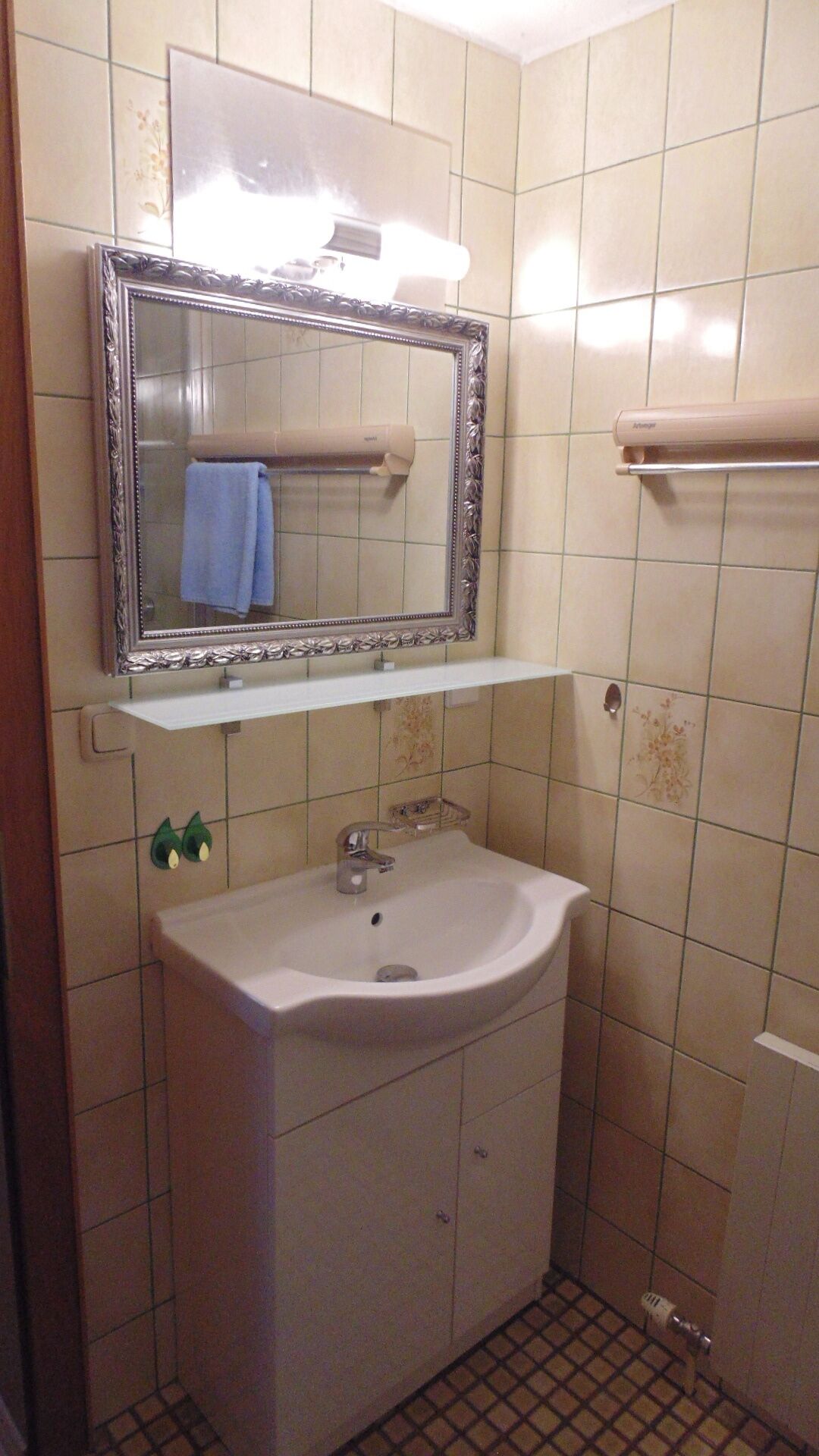 A bathroom with a white sink, a mirror with a decorative frame, and a towel hanging on a towel rack.