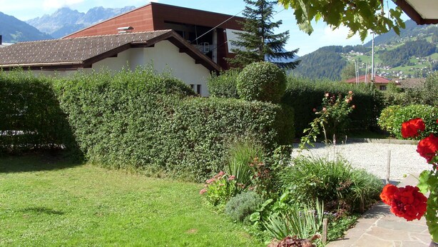 Una casa con techo inclinado, rodeada de un jardín cuidado con diversas plantas y flores.