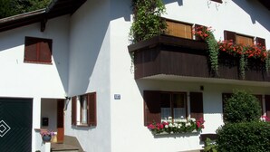 Un edificio de dos pisos con fachada blanca, contraventanas de madera y jardineras en los balcones.