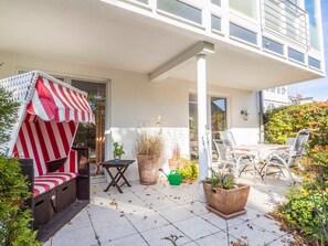 A covered outdoor seating area with a striped awning, a table, chairs, and potted plants.