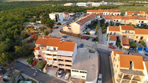 An aerial view of a residential area with multiple two-story buildings, a central road, and surrounding greenery.
