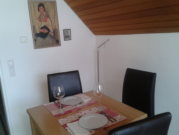 A dining table set with plates, cutlery, and wine glasses, with a painting and a small framed picture on the wall above.