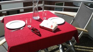 Ein Tisch im Freien mit roter Tischdecke, zwei Tellern, einer Karaffe, Gläsern und einer Taschentuchbox.