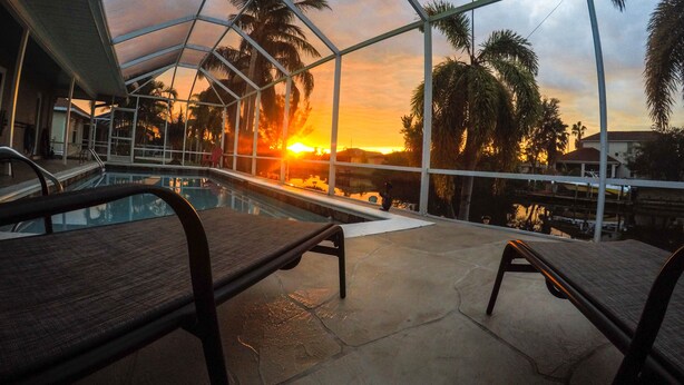A pool area with a glass ceiling, lounge chairs, and a sunset view.