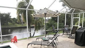 A covered outdoor area with a pool, lounge chairs, a table with chairs, and a view of a body of water.