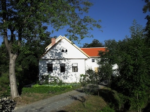Surrounded by lush greenery, this charming building features a simple facade with two windows and a chimney.