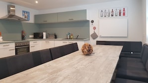 Une cuisine moderne avec des meubles blancs, un four encastré et un coin repas comprenant une table en bois et des bancs noirs avec des coussins.
