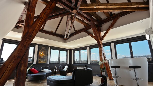 A spacious living area with a modern black sofa, a white bar area, and large windows offering a city view.