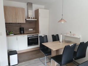 Une cuisine compacte équipée d’une cuisinière, d’un four et d’un évier, ainsi que d’une table à manger avec des chaises et d’un luminaire suspendu.