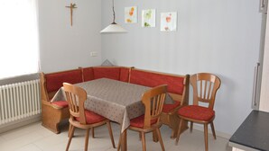 Un coin repas avec une table et six chaises en bois dotées de coussins rouges, un lampadaire blanc au plafond et trois œuvres d’art encadrées accrochées au mur.