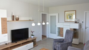 Un salon moderne avec un téléviseur à écran plat, un fauteuil gris et un meuble de rangement en bois.