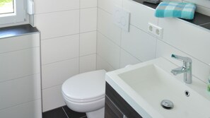 A modern bathroom with a white toilet, a white sink with a chrome faucet, and a towel hanging on the wall.