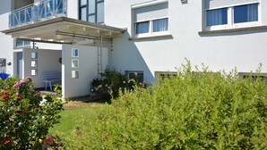Un bâtiment moderne à deux étages, doté d’un balcon, d’une entrée couverte et d’un jardin agrémenté de fleurs.