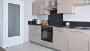 Une cuisine moderne avec des meubles de couleur bois clair, un plan de travail noir, un four encastré et un four à micro-ondes.