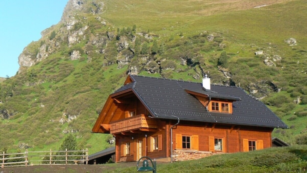 Una cabaña de madera con balcón, frente a un paisaje montañoso.
