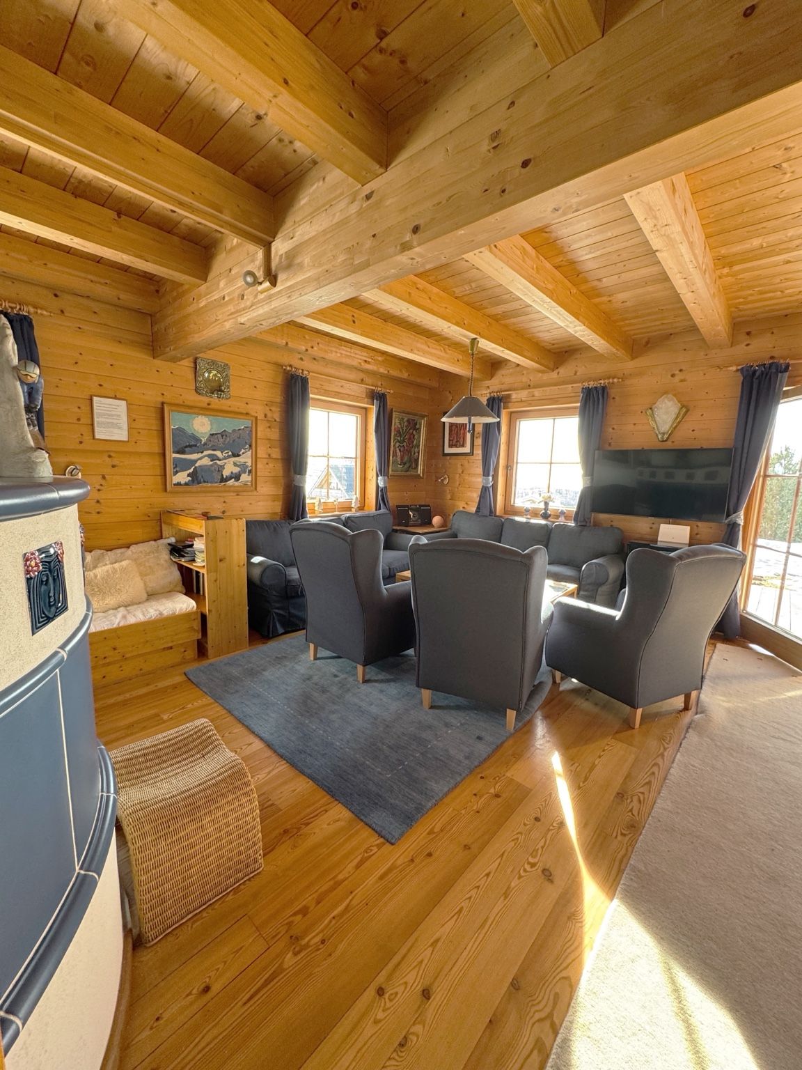Ein gemütliches Blockhaus-Interieur mit Holzwänden und -decke, einem Kamin, einer Sofagarnitur und einem Esstisch.