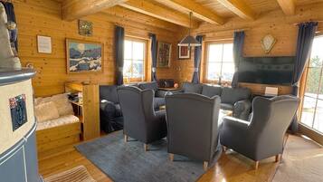 Ein gemütliches Blockhaus-Interieur mit Holzwänden und -decke, einem Kamin, einer Sofagarnitur und einem Esstisch.