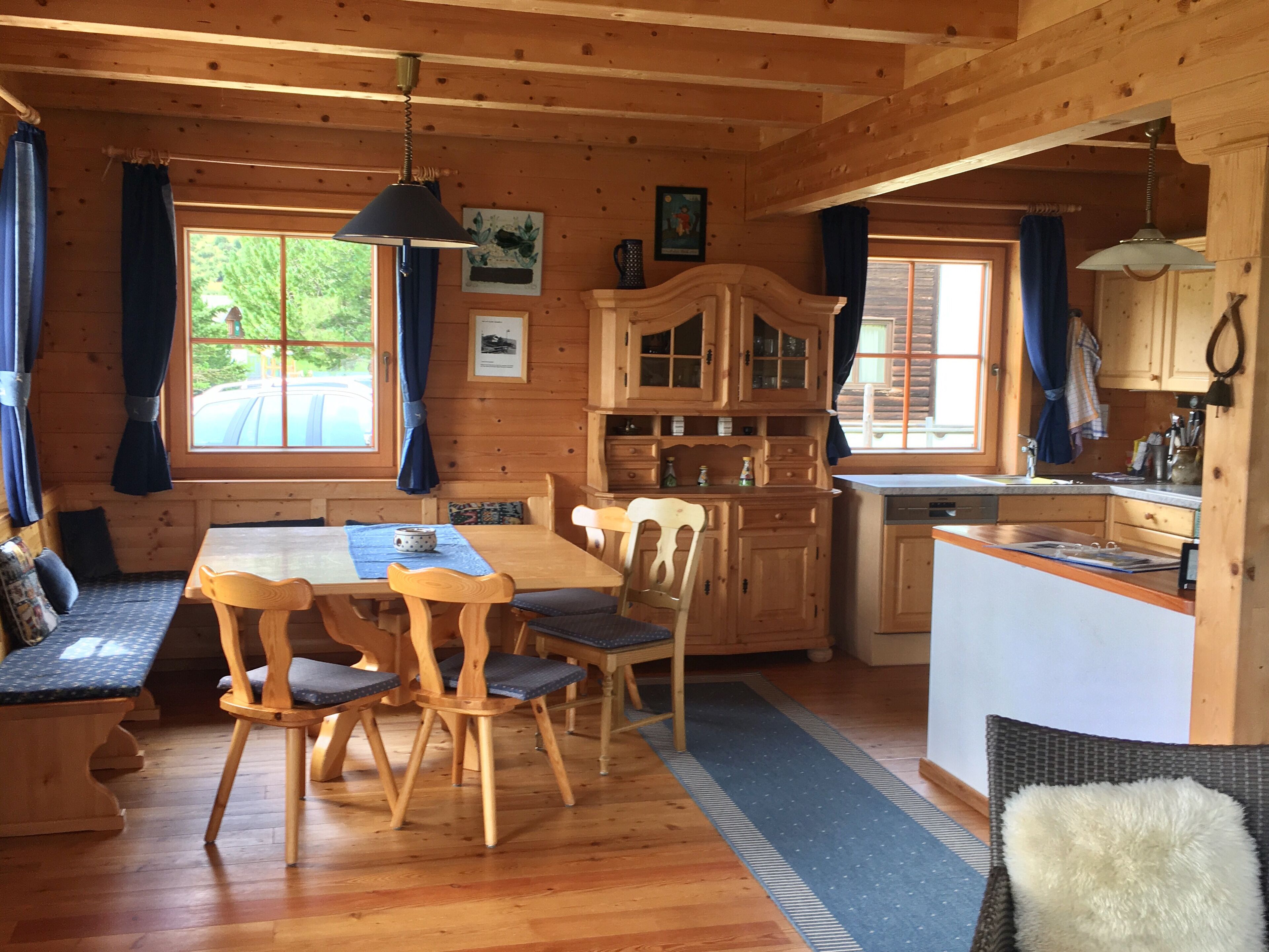 L’intérieur d’un chalet en bois comprend une table à manger, des chaises, un coin cuisine et offre une vue sur l’extérieur grâce à de grandes fenêtres.