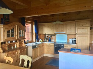 Une cuisine de style rustique, avec des meubles en bois, un évier, une cuisinière et un coin repas comprenant une chaise.