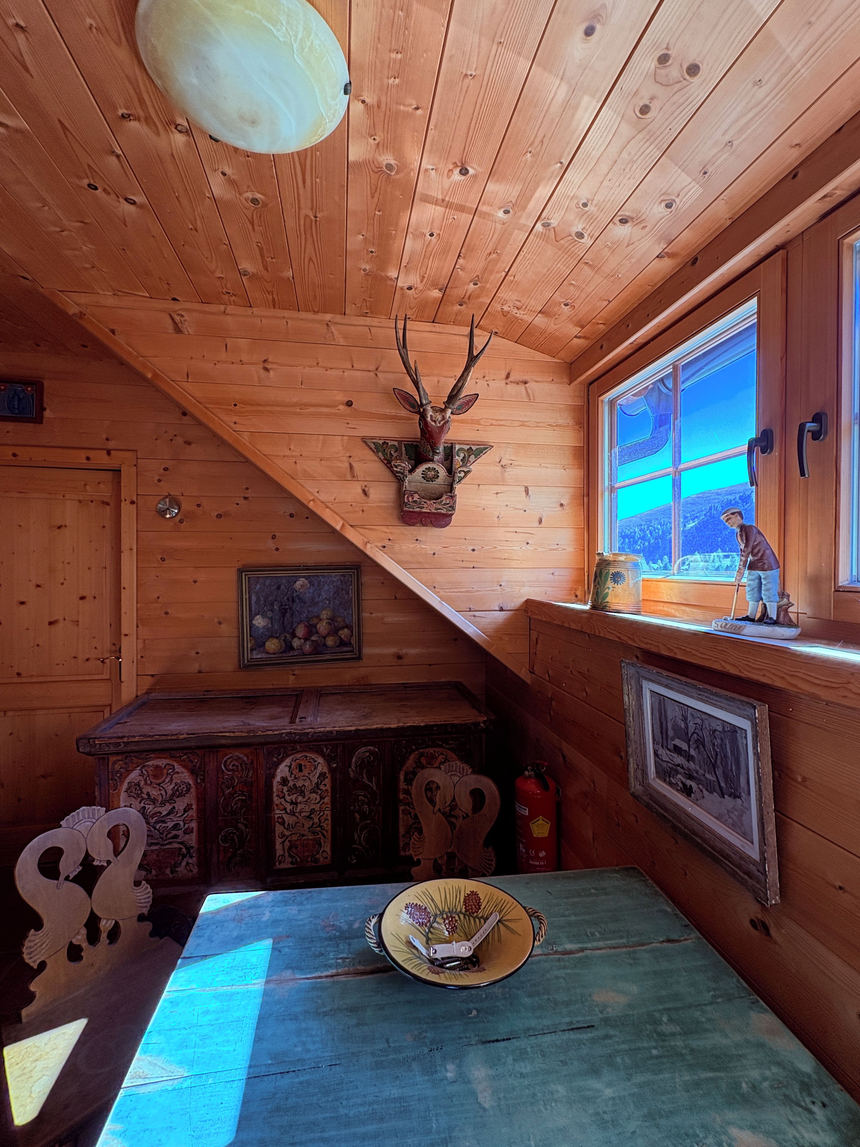 Ein Holzblockhaus-Interieur mit einem aufgehängten Hirschkopf, einem Tisch mit einem Hut und einem Fenster mit Blick.