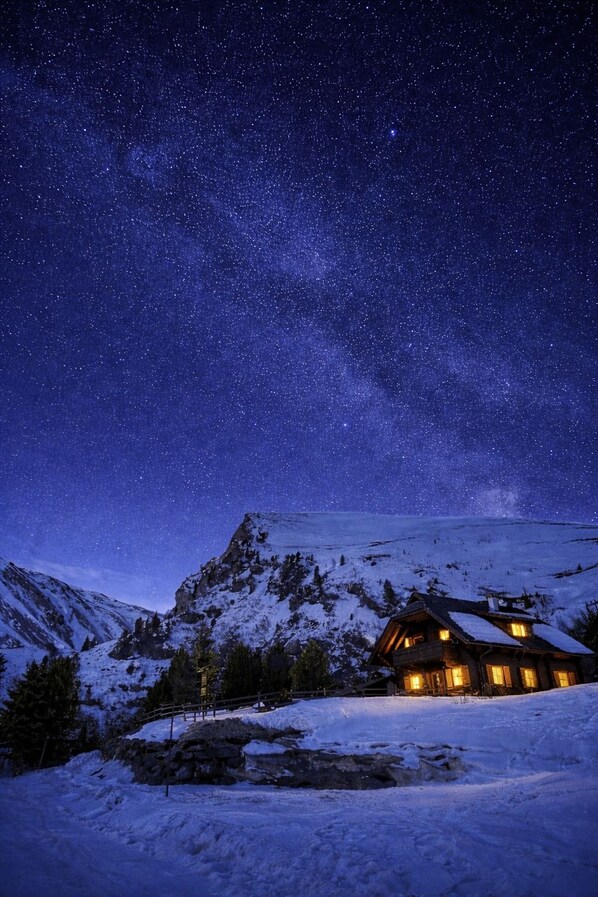 A snow-covered mountain with a wooden cabin illuminated by warm lights.