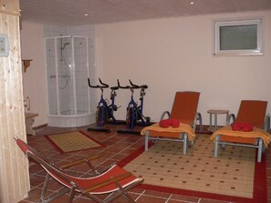 Une pièce équipée d’une douche, de deux vélos d’exercice et de deux fauteuils.