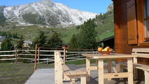 Una cabaña de madera con terraza y mesa de picnic, con vistas a una montaña y cielo despejado.