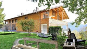Una casa moderna con terraza de madera, un trampolín y un pequeño jardín.