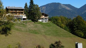 Un edificio de varios pisos con balcones, rodeado de árboles y montañas.