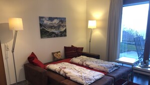 Un dormitorio con cama, mesitas de noche, una ventana con vistas y un cuadro en la pared.