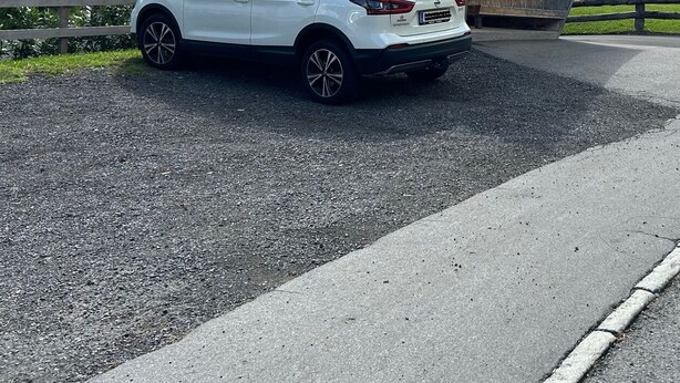 Un SUV blanco estacionado en una carretera, con una estructura de madera al fondo.