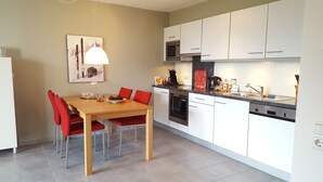 Cocina moderna con armarios blancos, microondas y estufa. Hay una mesa de comedor con sillas rojas y una lámpara colgante.