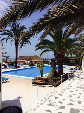 A pool area with lounge chairs and a bench, surrounded by palm trees.
