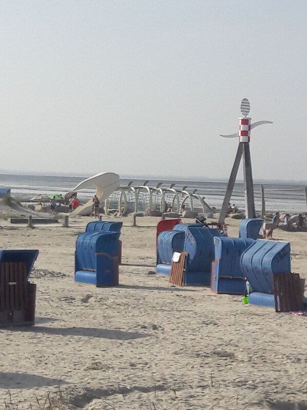 Une plage avec des chaises longues bleues et une grande structure blanche surmontée d’un toit rouge et blanc.