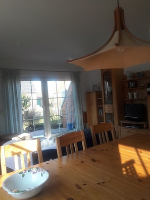 Un coin repas avec une table en bois, des chaises, un saladier, un téléviseur et une bibliothèque.