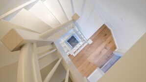 Una escalera blanca que conduce a una habitación con suelo de madera y una pequeña ventana.