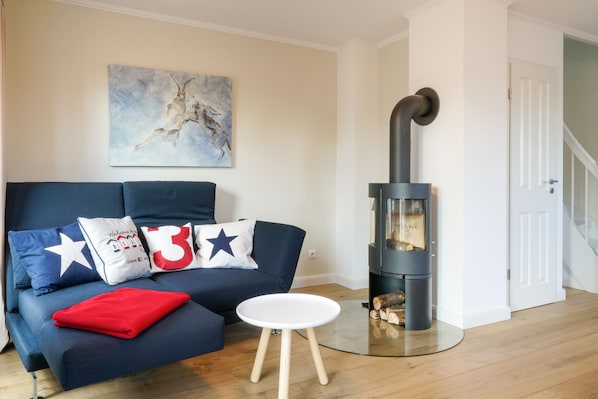A living room with a blue sofa, a white coffee table, and a wood-burning stove. - Vacation home in Dorf - beach chair on the beach and at the house (Sankt-Peter-Ording)