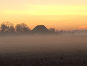 A rural landscape with a house silhouetted against a sunset. - Vacation home in Dorf - beach chair on the beach and at the house (Sankt-Peter-Ording)