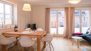 Una sala de estar moderna con una mesa de comedor de madera, sillas blancas, un televisor y un sofá con una manta roja.