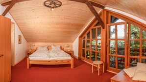 Une chambre confortable avec un plafond en bois, un lit, une table de chevet, une petite table et de grandes fenêtres donnant sur l’extérieur.