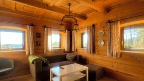 L’intérieur d’un chalet accueillant, avec un plafond en bois, un canapé, une table basse et deux fenêtres avec des rideaux.