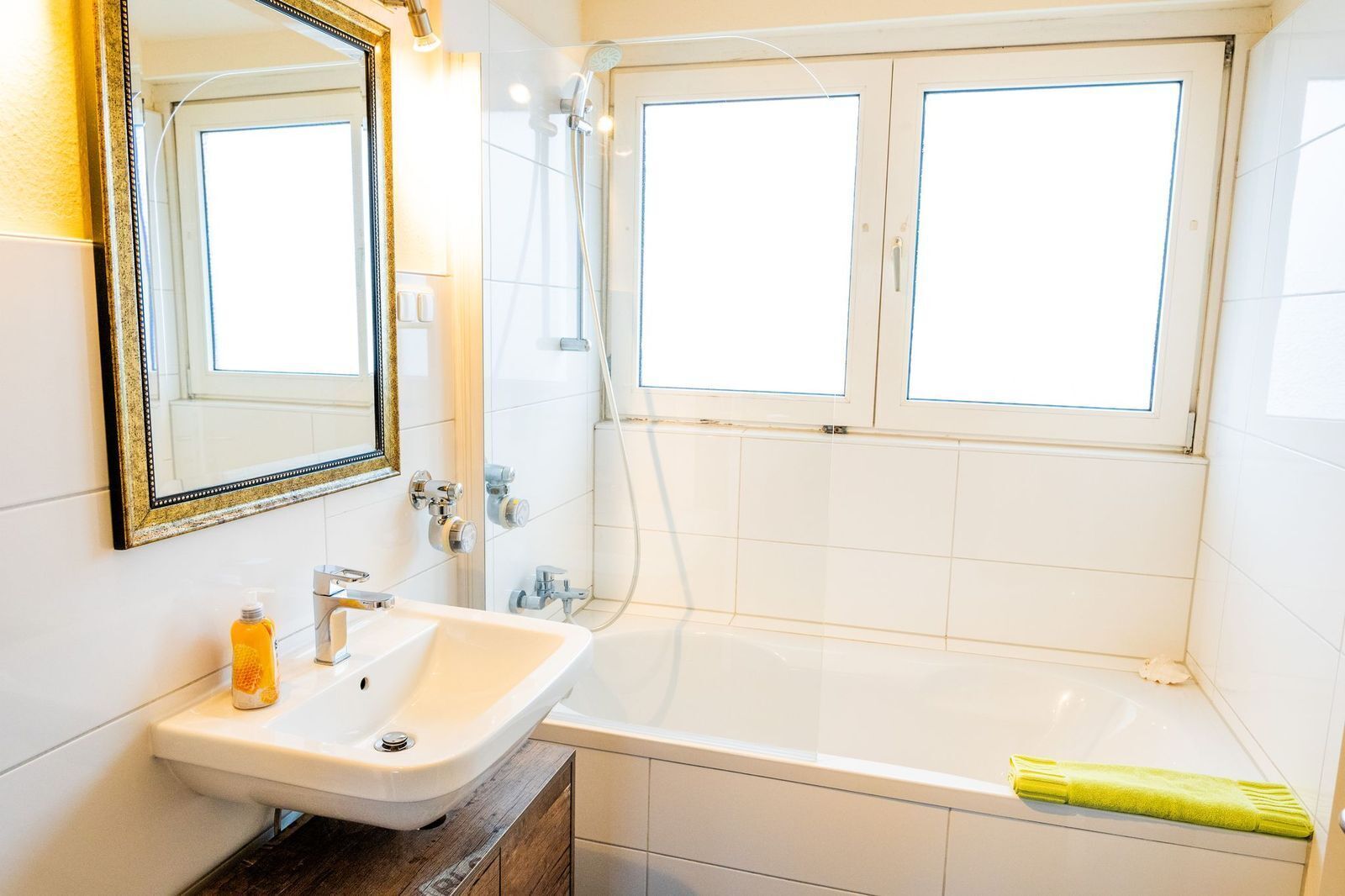 A bathroom with a white sink, a mirror, a shower, and a window.