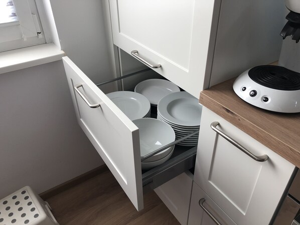 A kitchen with white cabinets, a wooden countertop, and a drawer with stacked plates.