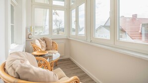 A sunlit room with a large window, wicker furniture, and a radiator.