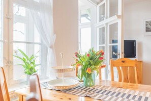 Ein Essbereich mit einem Holztisch, zwei Stühlen, einer Blumenvase, einem Tablettständer und einer Topfpflanze.