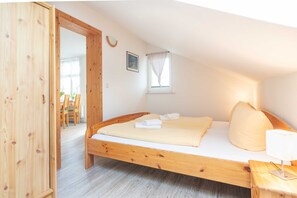 A wooden-framed bed with white linens, a bedside table with a lamp, and a window with a curtain.