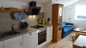Une cuisine compacte équipée d’un four encastré, d’un four à micro-ondes et d’un évier. On y trouve également une armoire en bois et un canapé bleu dans le salon attenant.