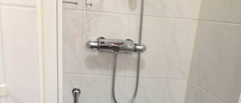 Piccola cabina doccia rivestita di piastrelle, con soffione a mano e rubinetto estraibile.