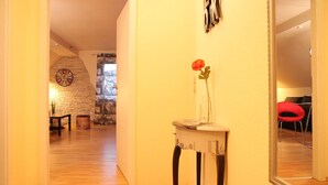 A hallway with a wooden floor, a stone wall, and a clock. There is a small table with a vase of flowers. - Large apartment (50m²), up to 4 pers., quiet, close to the city center, south-facing balcony, parking spaces (Niestetal)
