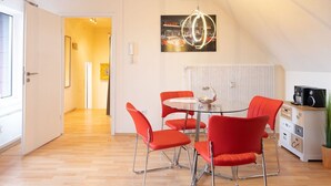 A modern kitchen with a round table, red chairs, and a hanging light fixture. - Large apartment (50m²), up to 4 pers., quiet, close to the city center, south-facing balcony, parking spaces (Niestetal)